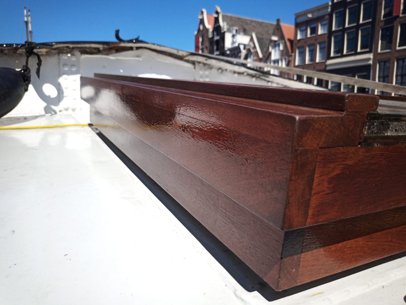 Restored varnished hardwood boat coaming with Amsterdam canal houses behind it