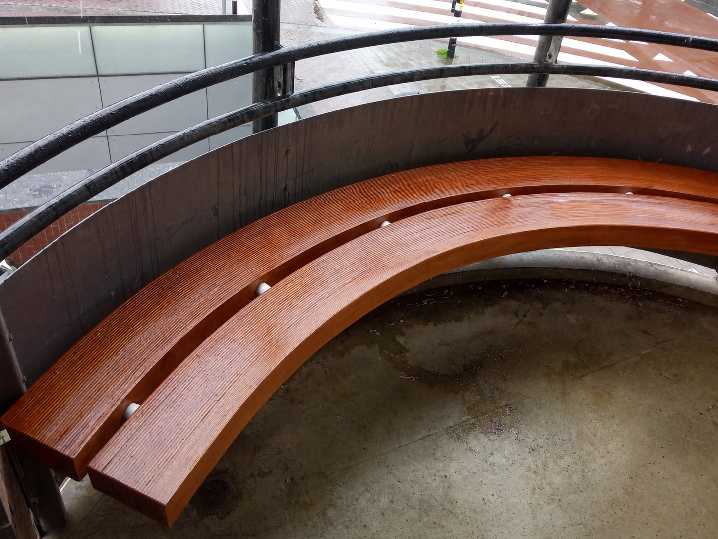 Completed curved timber bench with a warm varnished finish beside a large window