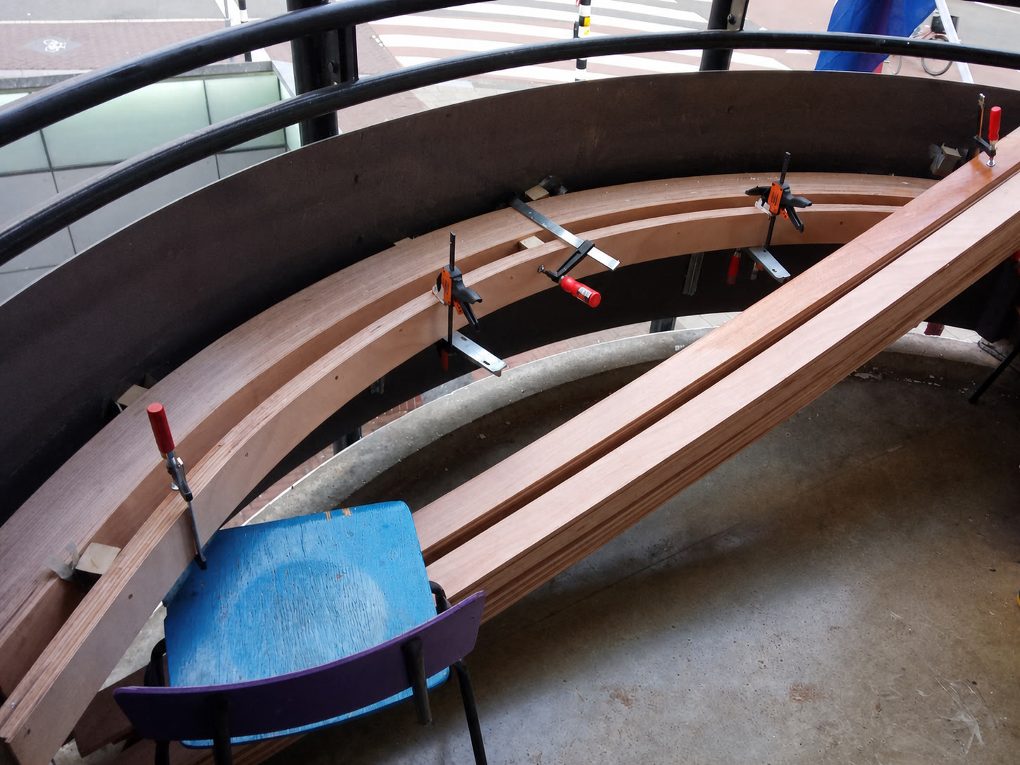 Curved timber bench being assembled and clamped in place beside a large window